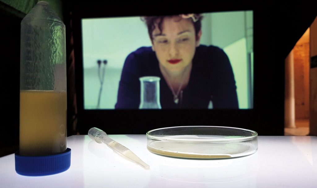 A woman on a screen looks at the petri dish of "female sperm" before her