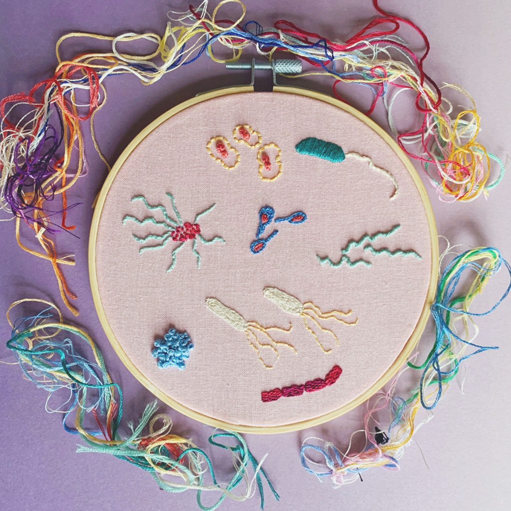 Embroidery piece with multiple types of colorful bacteria, surrounded by scrap embroidery thread.  