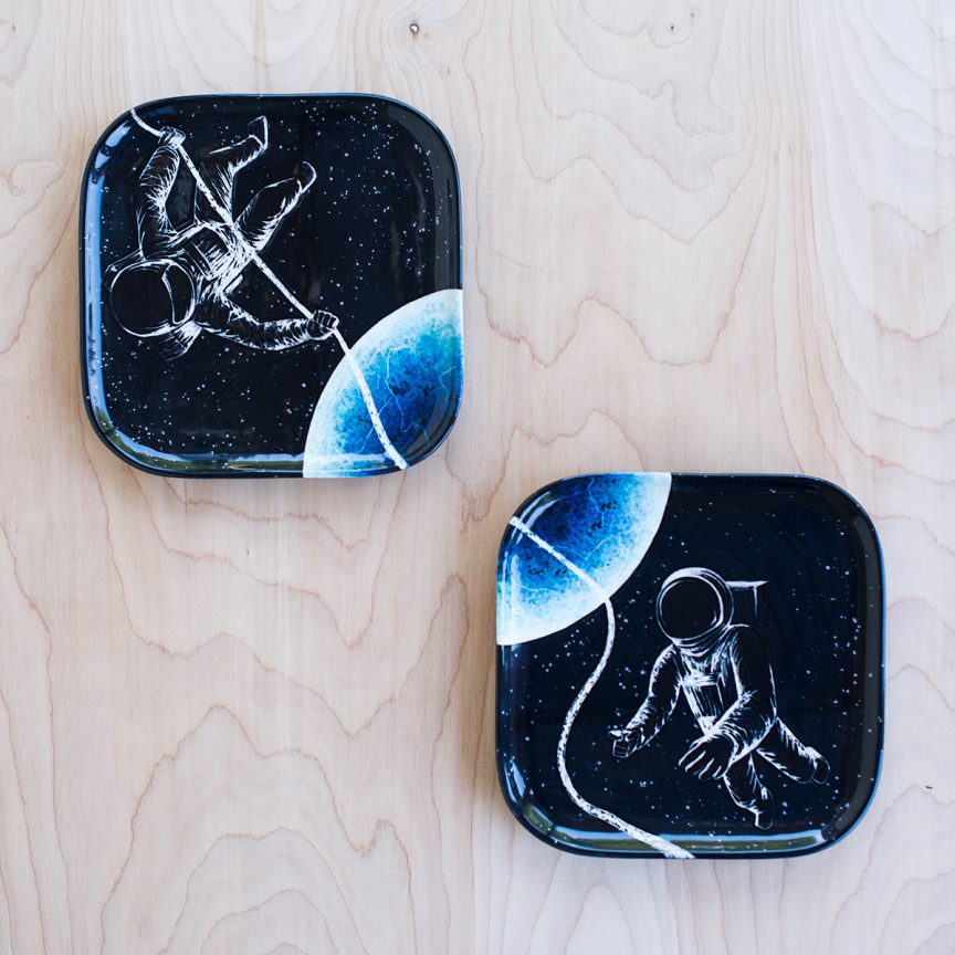 Two square plates with their corners close together diagonally. They each depict astronauts in space trying to hold onto a rope to connect them.