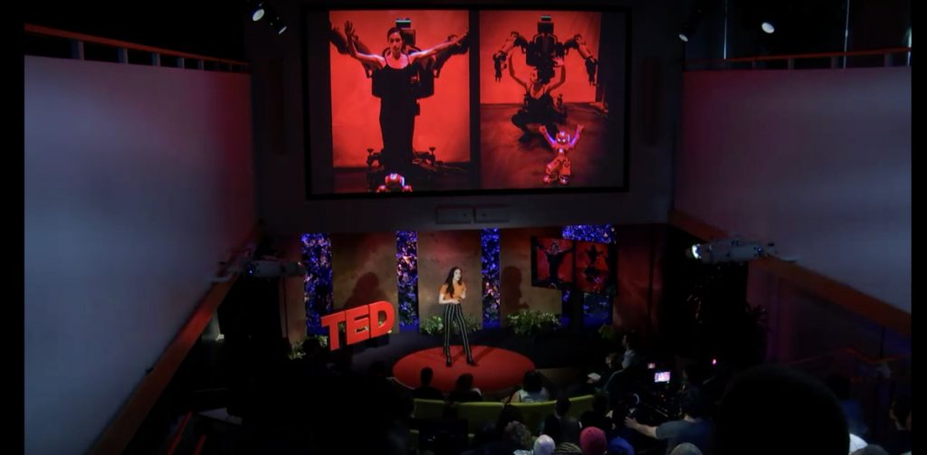 Catie talking on the TED talk stage. Above her are large images from her projects.  