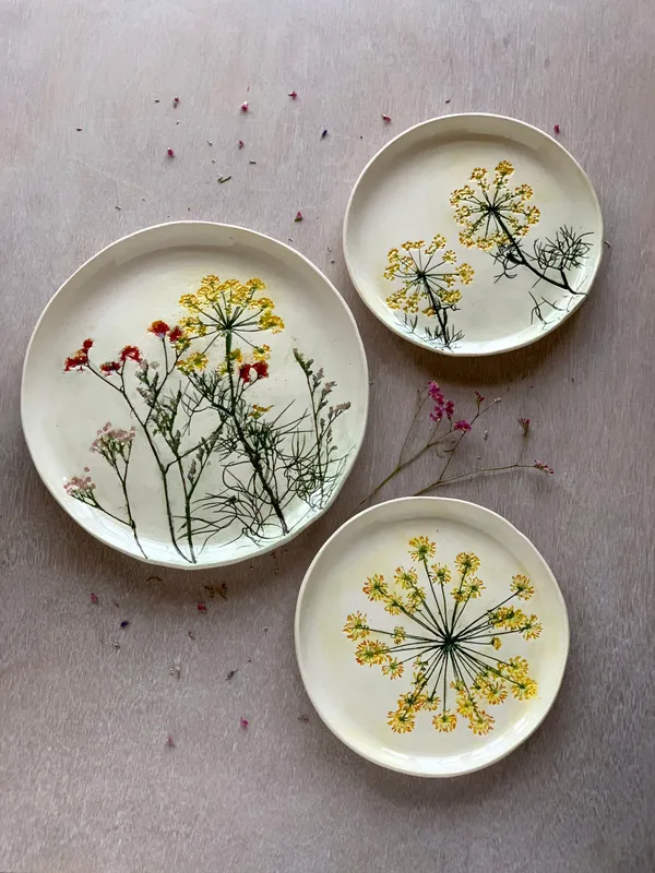 Three white plates with imprints of dill flowers. The flowers have been painted yellow, red, and pink.