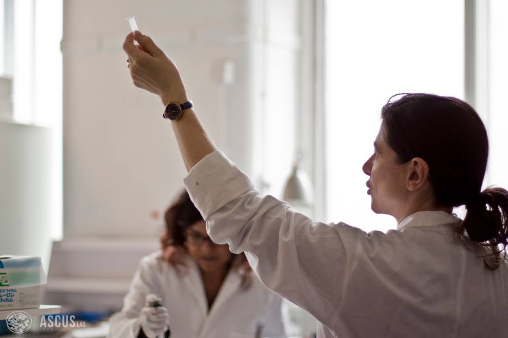 Woman wearing a lab coat holds up a small tube. 