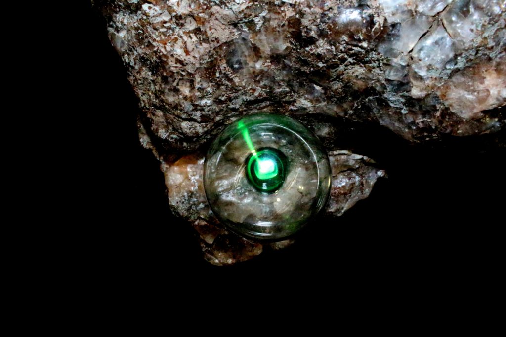 Rock with small green light covered by a clear, round plastic shield. 