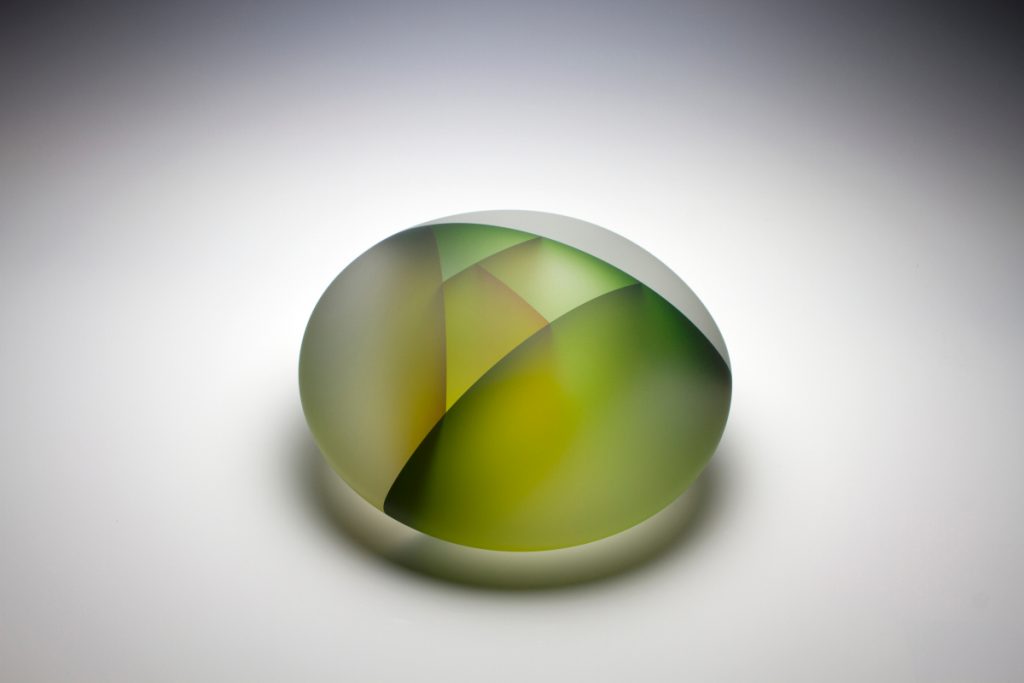 Green pebble shaped translucent glass structure depicting cell division displayed on a white background