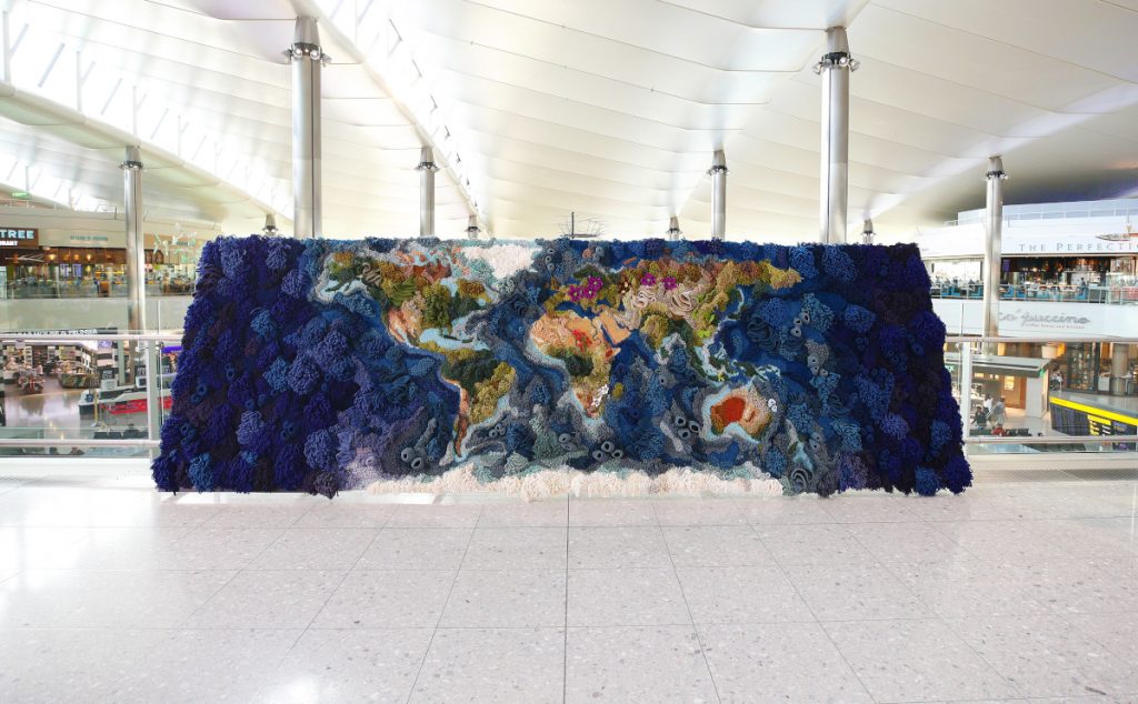 The Botanical tapestry, which shows a colorful world map and displays threatened flowers and corals. The tapestry is sitting in a terminal in Heathrow Airport. 