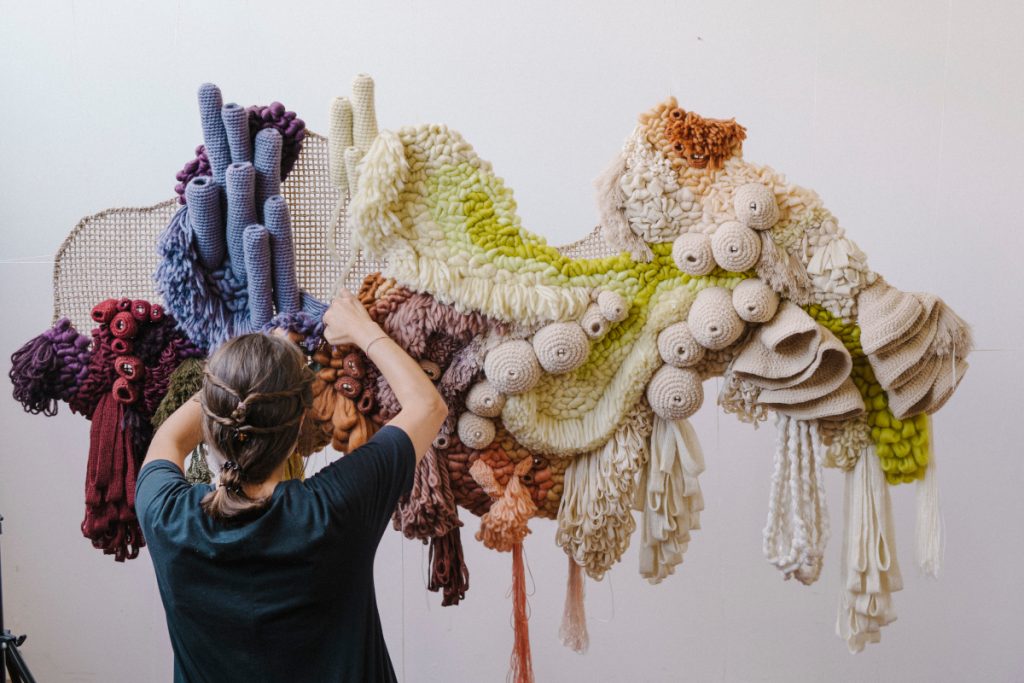 Vanessa working on one of her hanging tapestries which features colorful coral. 