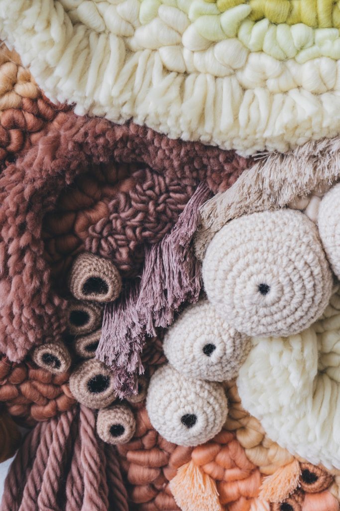 Close-up image of a tapestry showing coral and different yarns in varying red, white, and orange colors. 