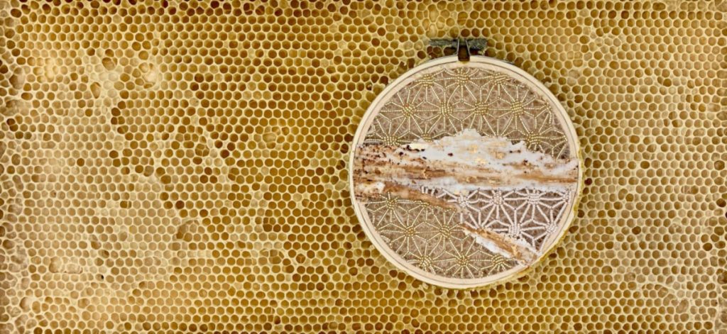 Circular embroidery hoop with cream and gold starburst pattern on tissue paper. The hoop is embedded in honeycomb. 