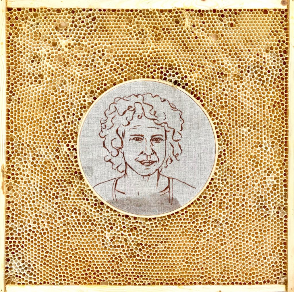 Self portrait of Ava Roth embroidered on linen in a circular embroidery hoop. The hoop is embedded in honeycomb. 