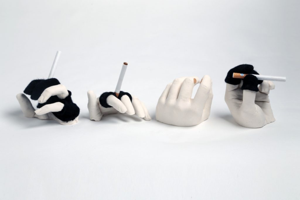 Four hands made of plaster wearing black knit garments and holding cigarettes. 