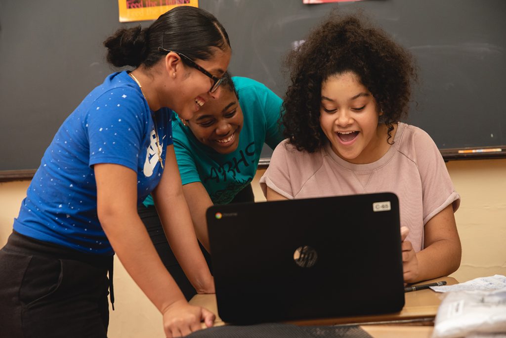 Three girls smiling while working on a laptop