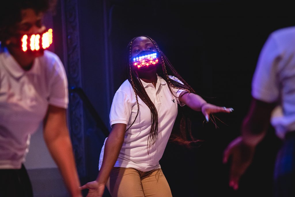 Girls dancing onstage with light-up face masks