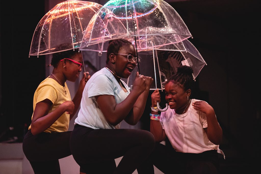 Three girls dancing while holding clear umbrellas with lighting at the top