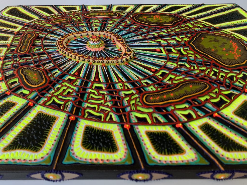A different angle of A Quiet Loud (2019) by Amie Esslinger. A vertically oriented rectangular work with large central cellular body that has an irregular oval shape. The very centre resembles a single scoop of ice cream. Multicoloured lines radiating out from it connect to an irregularly shaped ring of dots. The same lines start expanding as they go outward. They connect again through a porous red matrix. The pores are large and some are inhabited by more cellular bodies, coloured a swamp-like green with orange dots. Beyond the matrix is where the lines have extended and become their own bright yellow, triangular-shaped bodies within the whole work. This angle shows the 3D layering incorporated into the work.