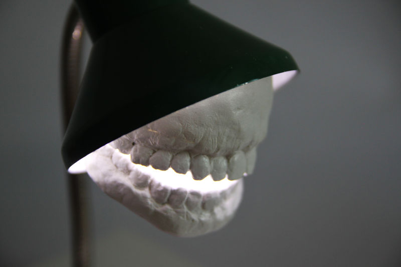 Molds of human teeth emerge from a desk lamp, making it look like it has a mouth. 