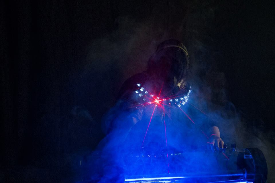 Woman looking downward wearing a mask that projects blue light into fog.
