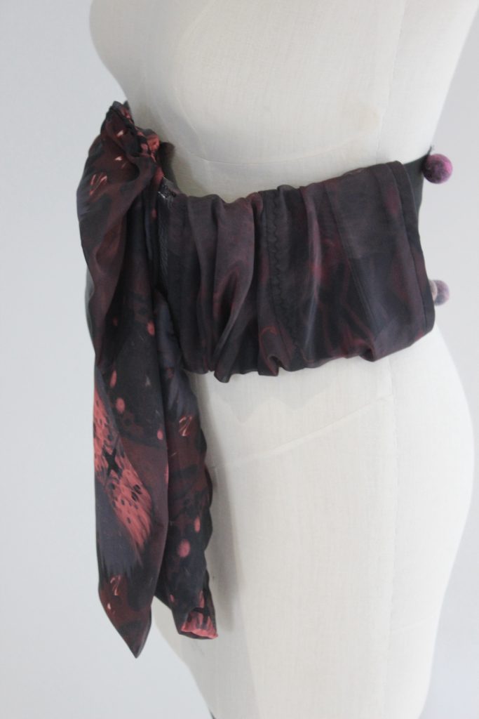 A photo of a mannequin with a large swathe of dark gathered fabric wrapped around its waist.