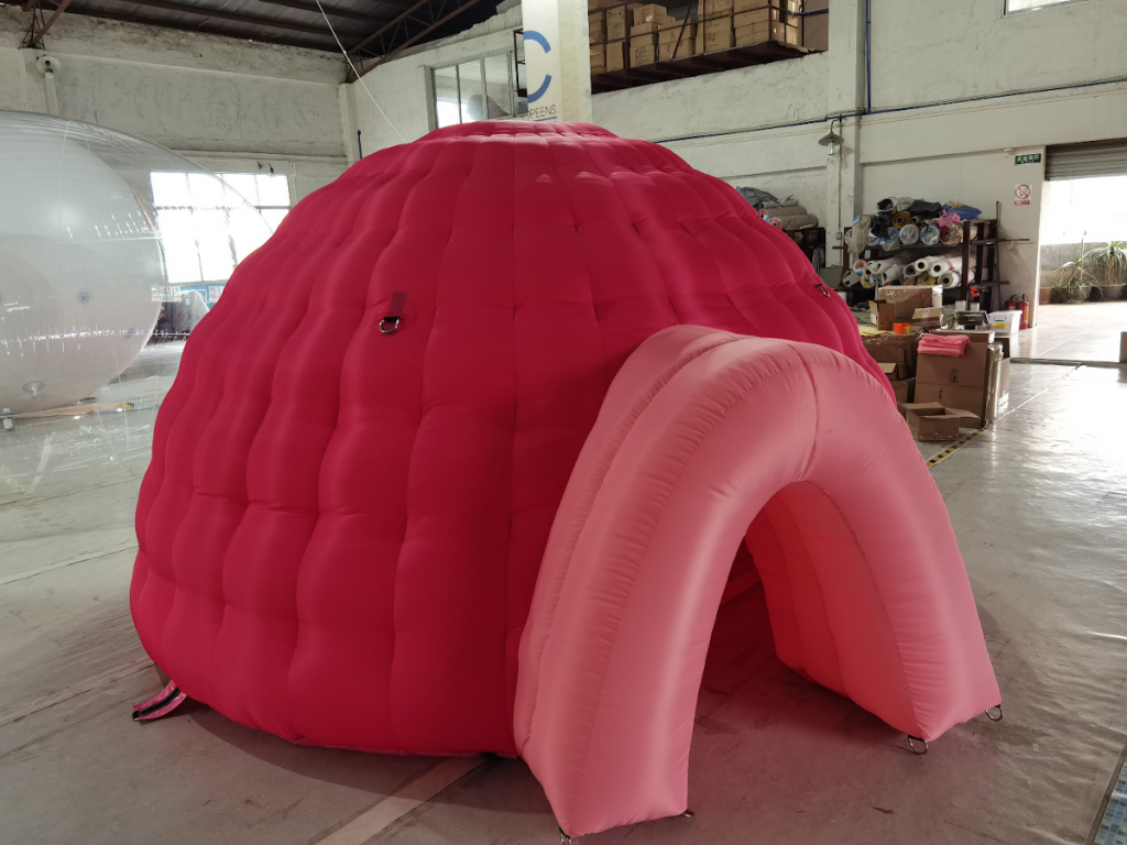 A photo of an inflated pink dome with an arched open entrance. The dome sits in a warehouse.