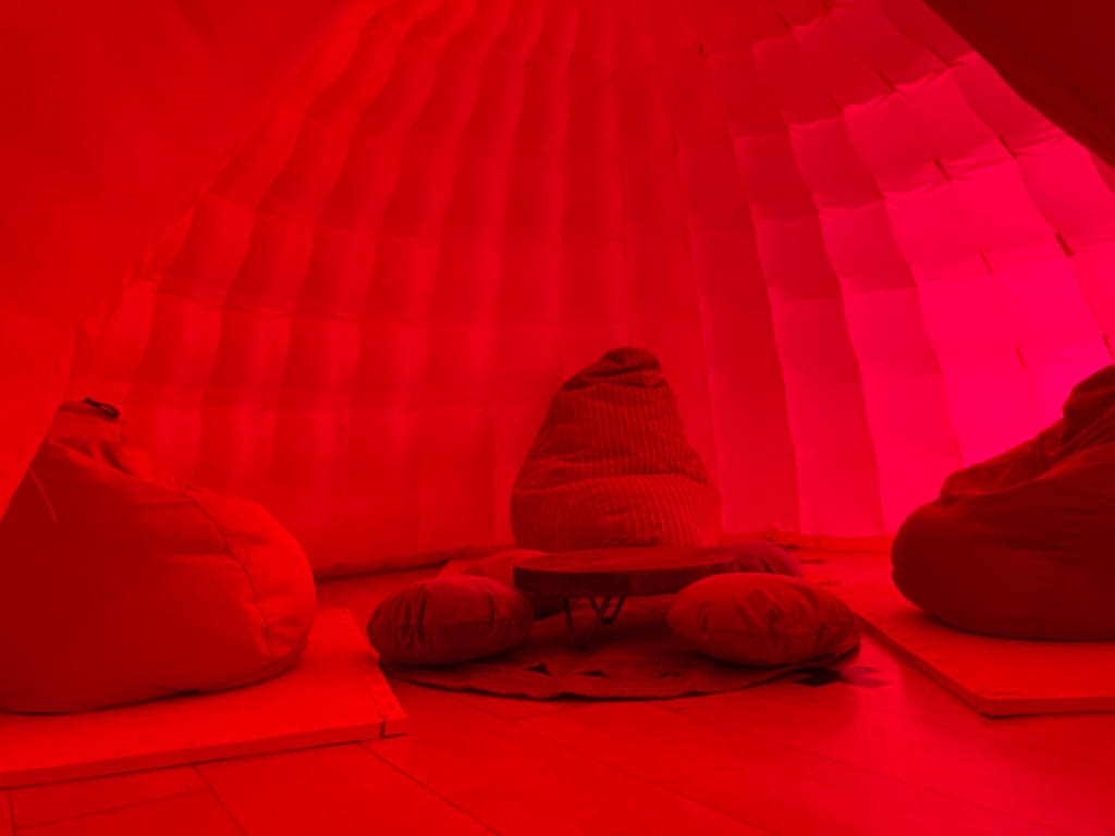 A photo of three bean bag chairs around a small table and small cushions. They sit inside a dark pink dome.