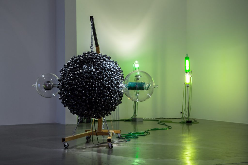 A large black sphere studded with small black structures conencted by cables to a green standing light.