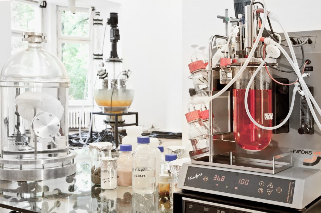 Biochemistry apparatuses with different colored liquids sit on a table in front of a white background.