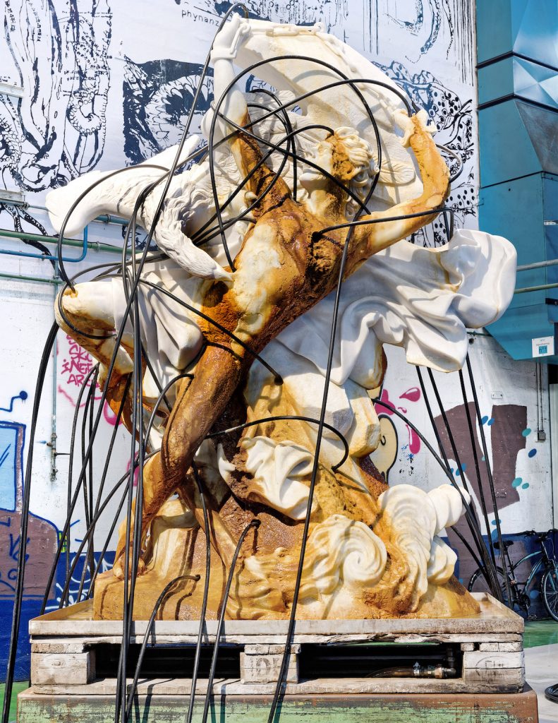 A marble sculpture of the figure of Prometheus, with black cables and copper-colored material spilling down the front.