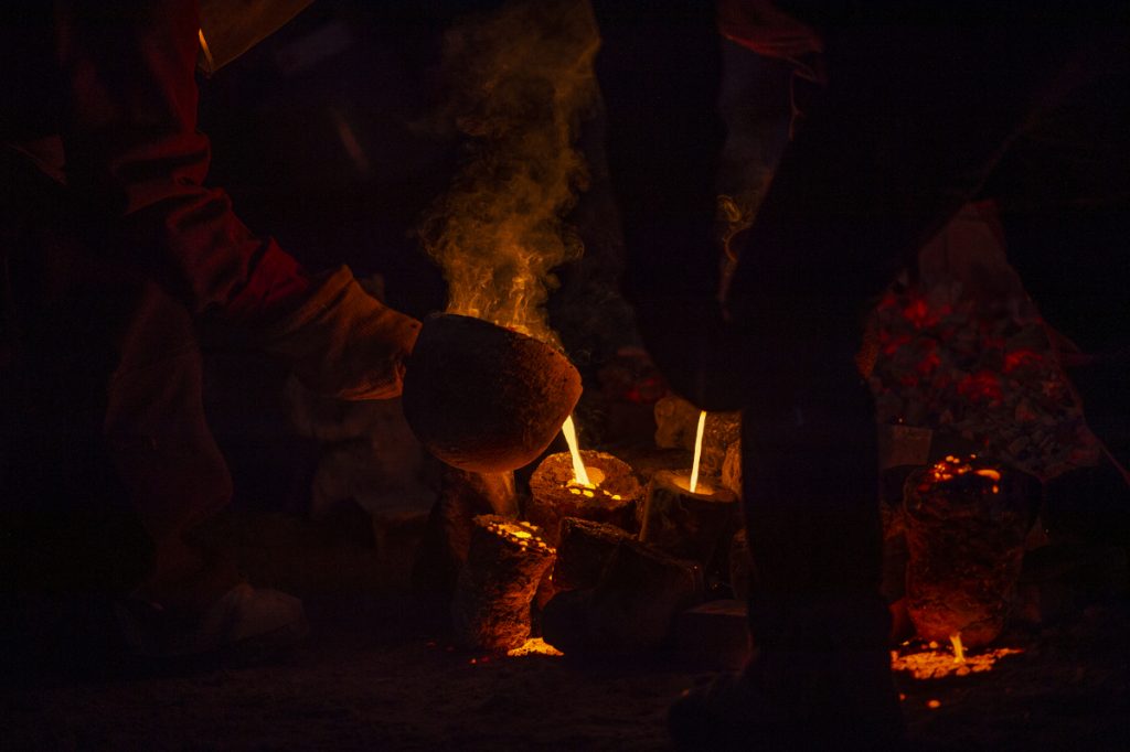 Two figures pour hot iron into organic moulds in the dark.