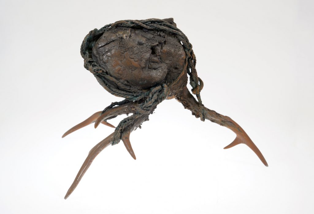 A brown, organic metal sculpture with rope detail and three branching legs.