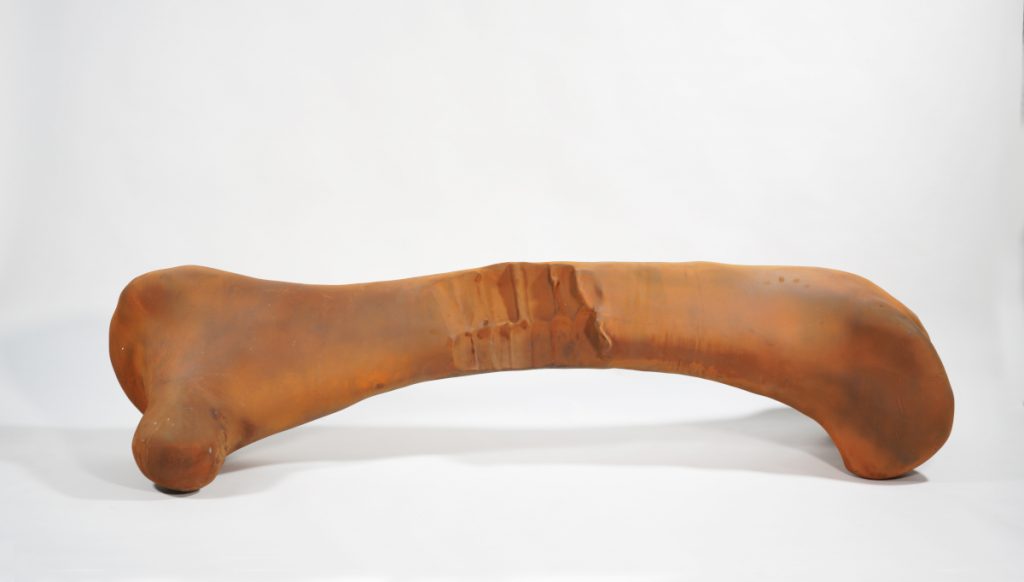 An orange metal sculpture of a bone with indentations in the middle.
