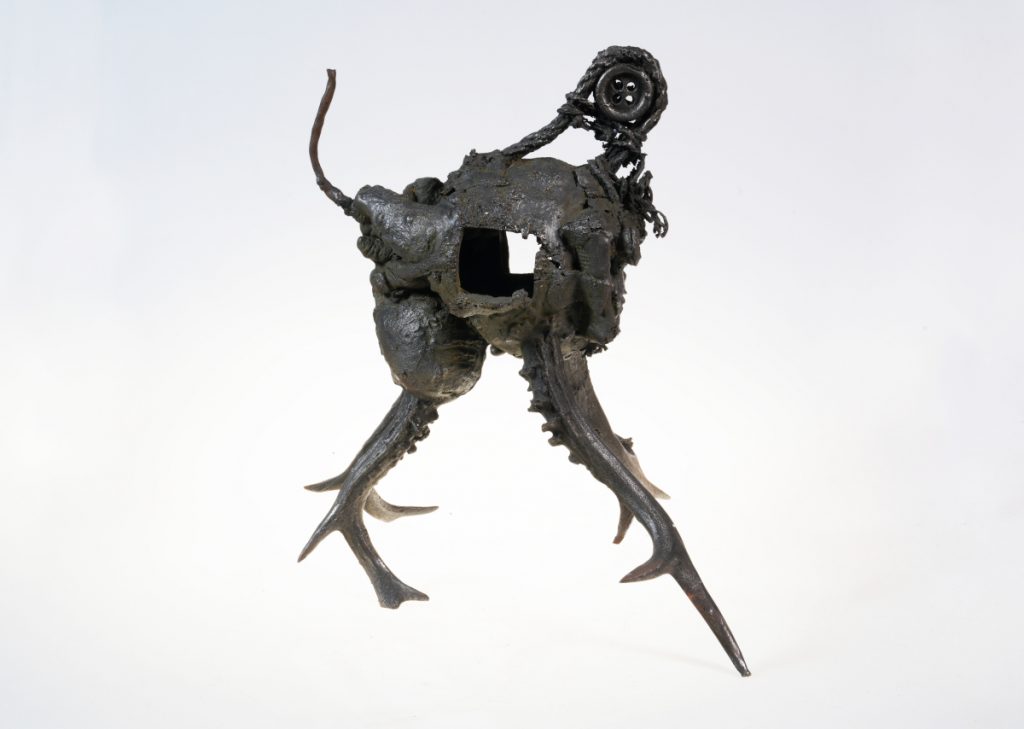 An organic, metal sculpture with two legs, and rope, button, and wire details.
