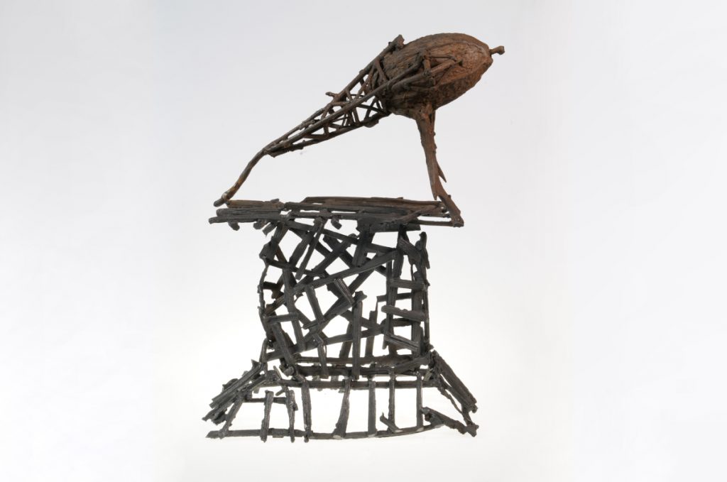 A lattice-like metal sculpture with a lighter-coloured mound balanced on top.