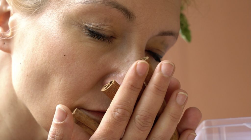 A woman with her eyes closed holds cinnamon sticks to her face and smells them