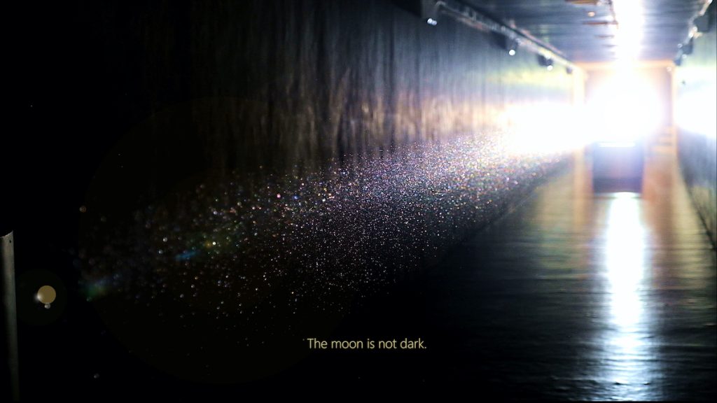 Dust illuminated in a tunnel. Uma legenda no fundo da imagem lê "A lua não é escura."