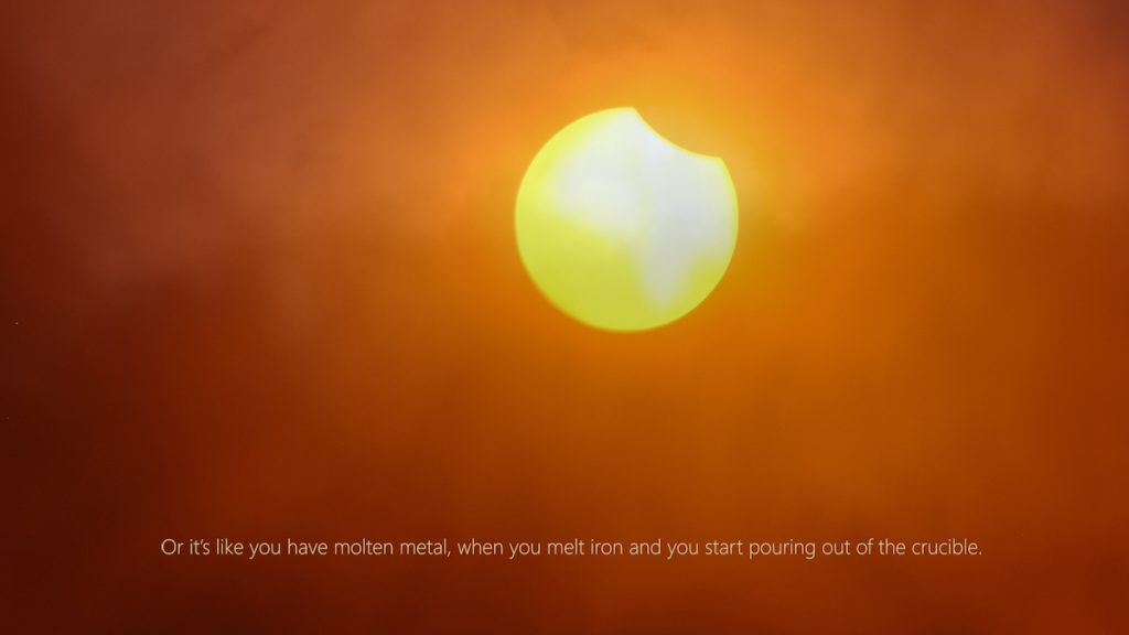 A bright yellow sun against an orange sky. The sun is just beginning to be eclipsed. A caption at the bottom of the image reads "Or it's like you have molten metal, when you melt iron and you start pouring out of the crucible."